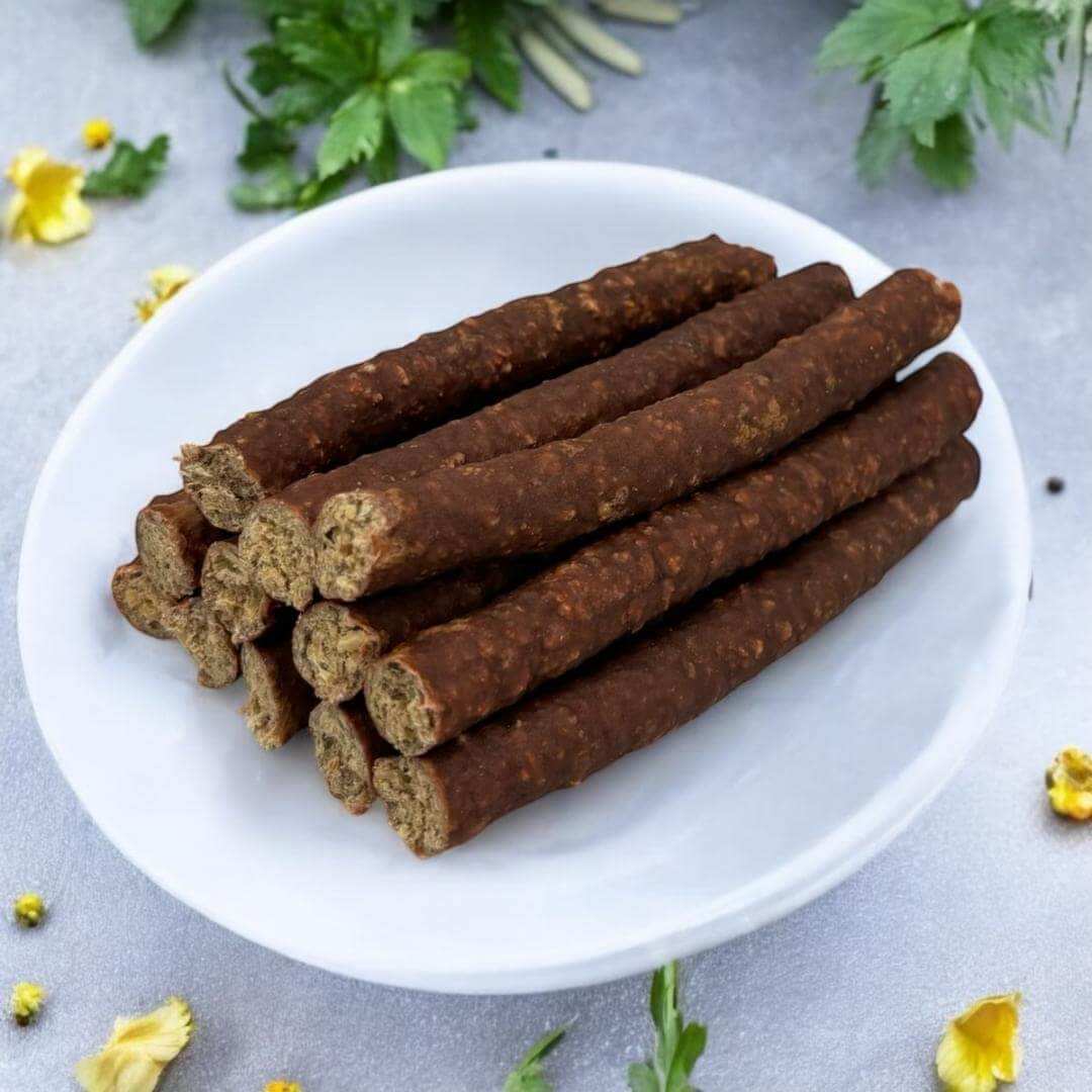 Photo of 12 turkey stix dog treats sitting on a white plate with yellow flowers and garnish around the plate.